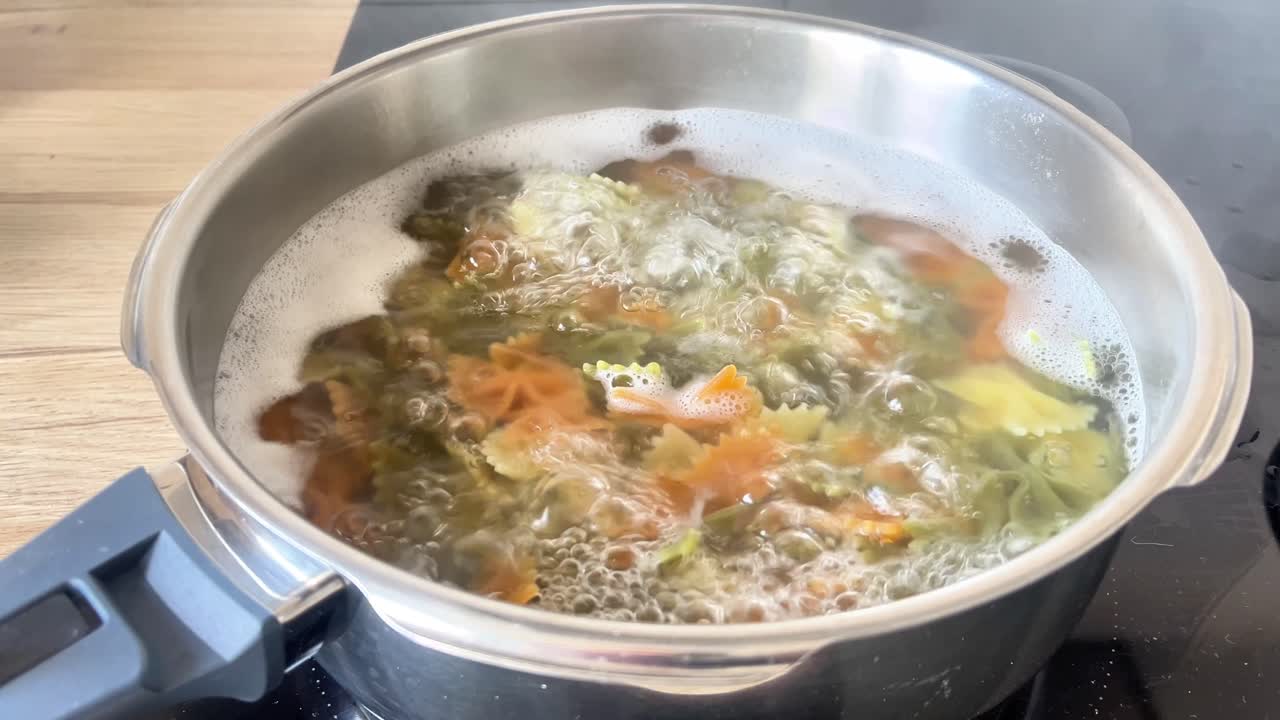 Una olla de sopa hierve en una estufa. La sopa es una mezcla de verduras y pasta