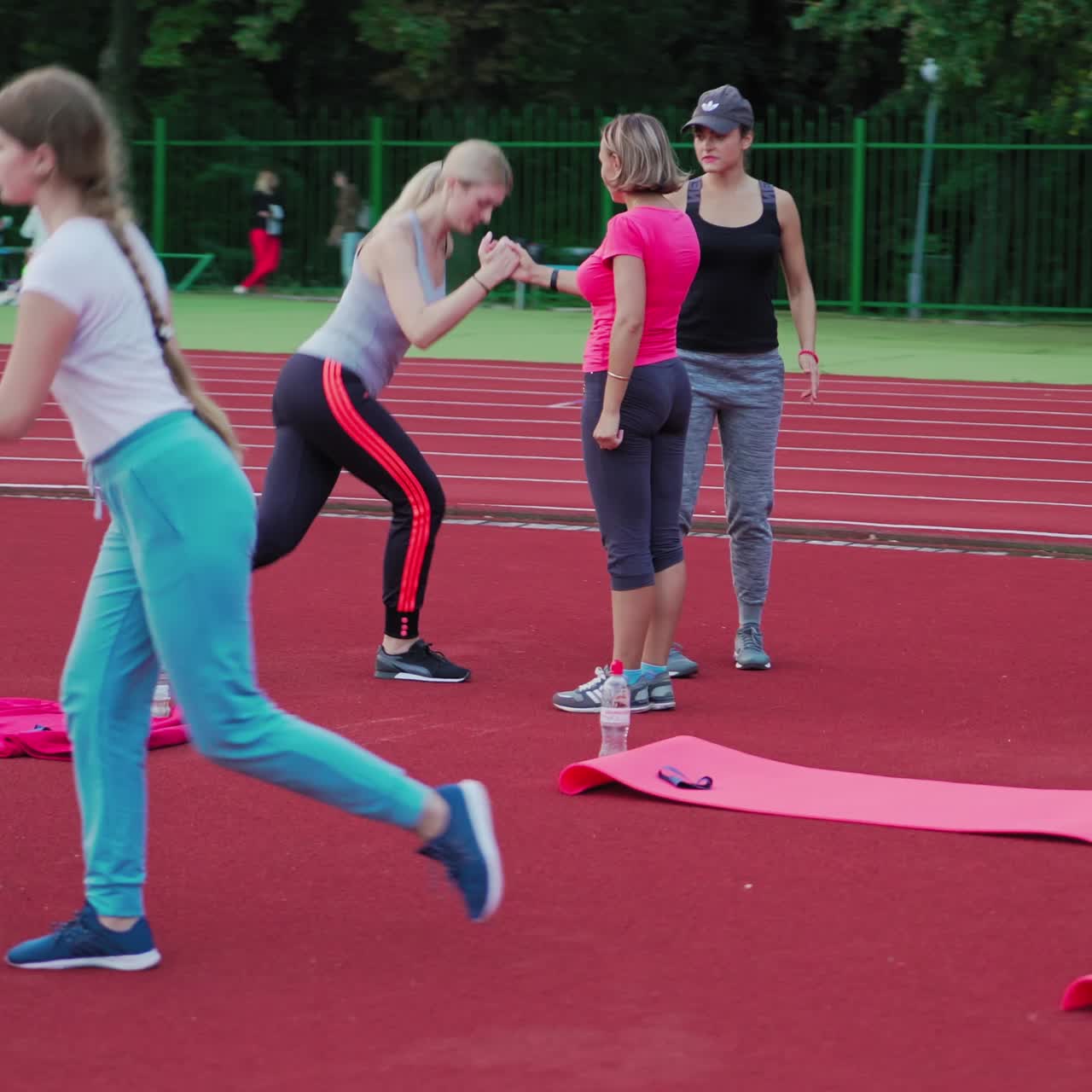 Young women doing fitness exercises in pairs outdoors. Fitness team of female in sportswear are training on the sportsground in summer.