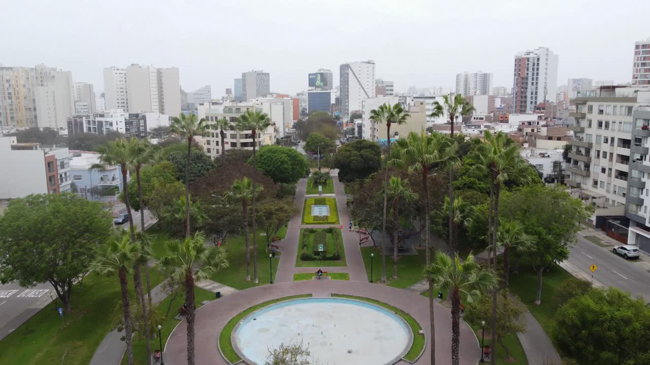 drone 4k video drone vuela hacia adelante y hacia arriba en un parque revelando muchos árboles, una fuente y muchos edificios en el fondo y el horizonte