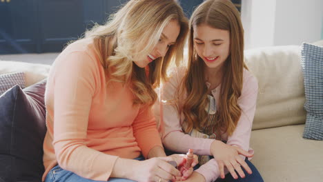 mother and daughter having fun sitting on sofa at home doing nails together