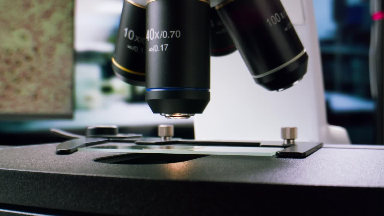 Scientist's Gloved Hand Adjusting Microscope Objective in a Laboratory