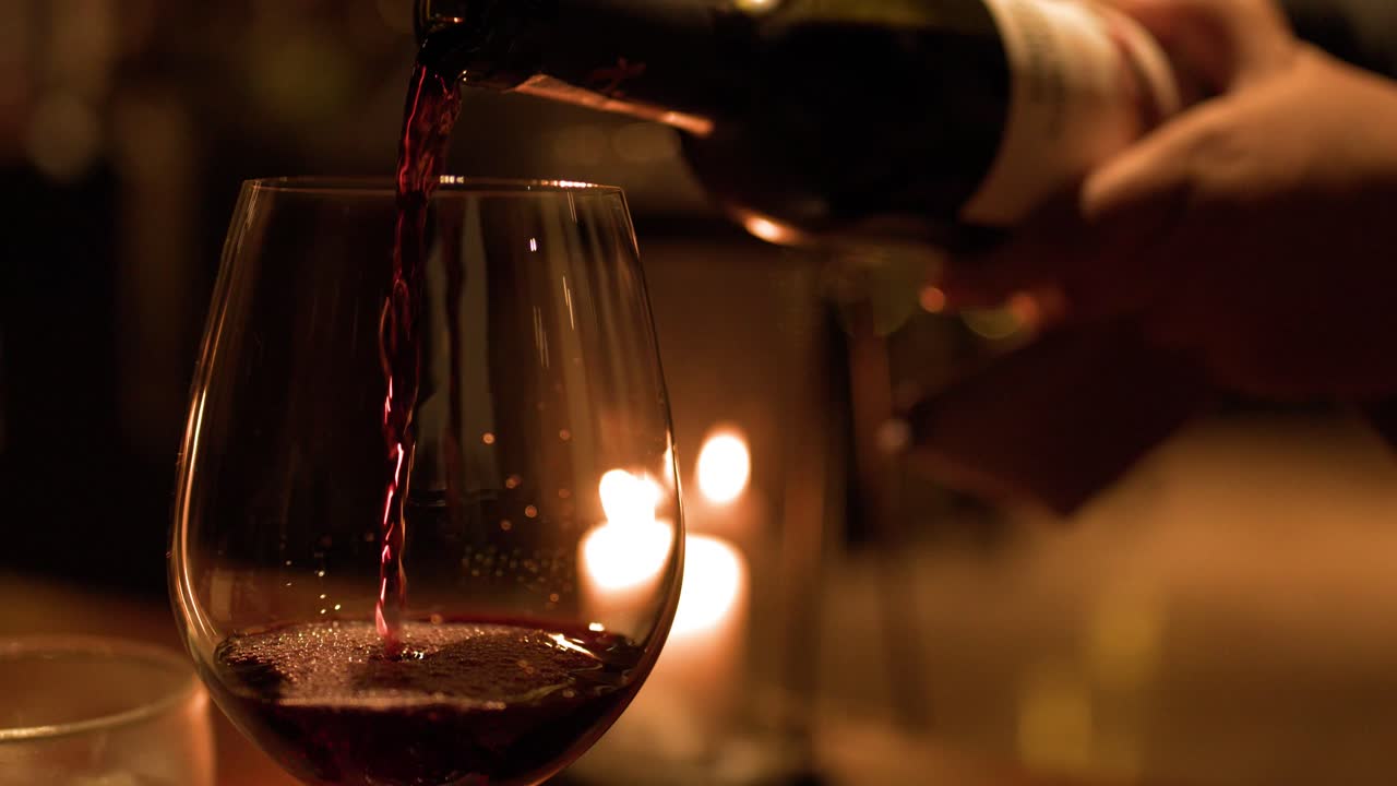 Primo piano di vino rosso versato in un bicchiere durante un'intima cena a lume di candela