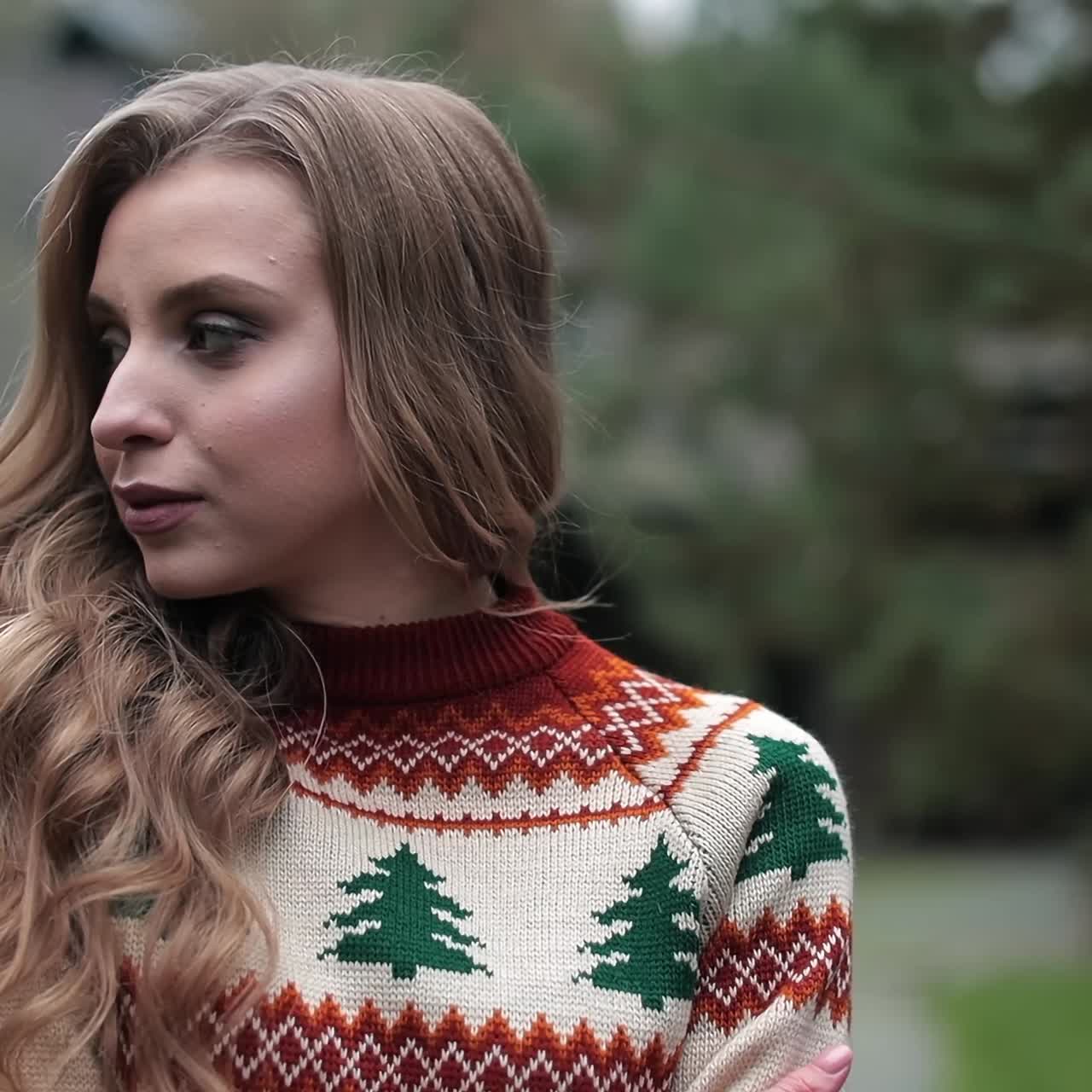 Attractive woman wearing warm sweater posing outdoors. Blonde lady standing outside. Wooden house and nature in blur at the backdrop