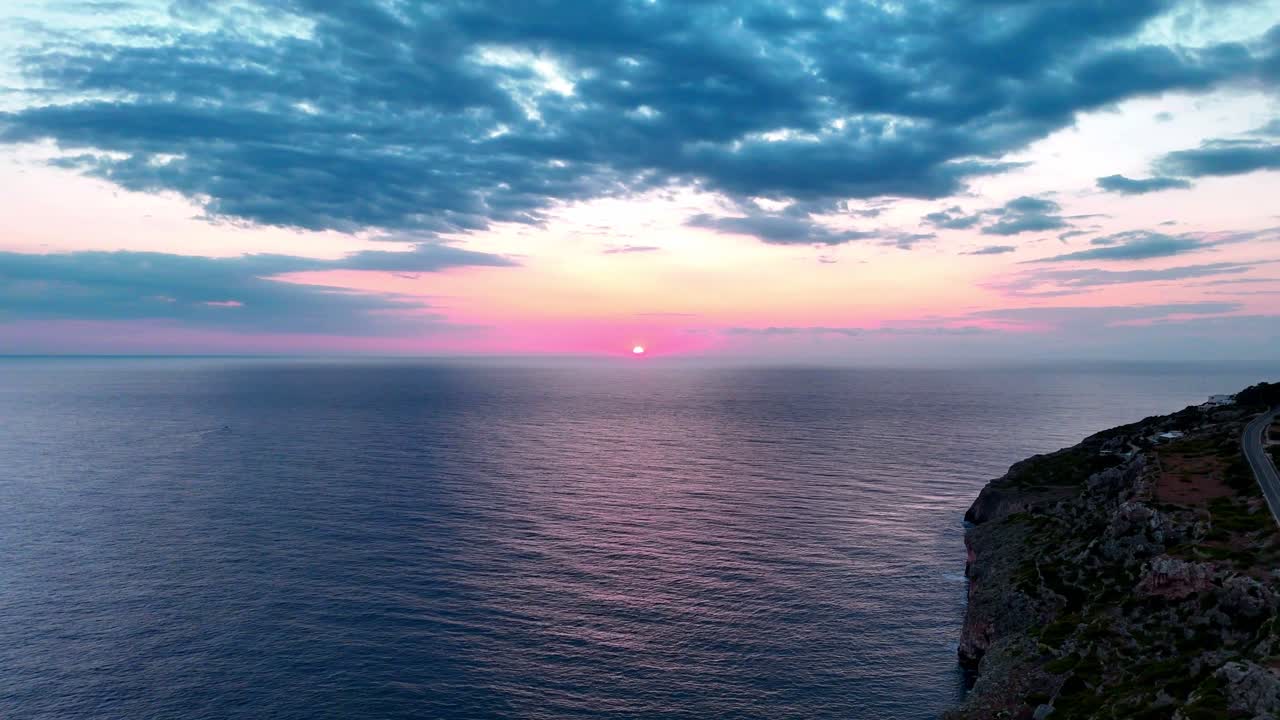 Pink sunrise over open water with cinematic cloud layers