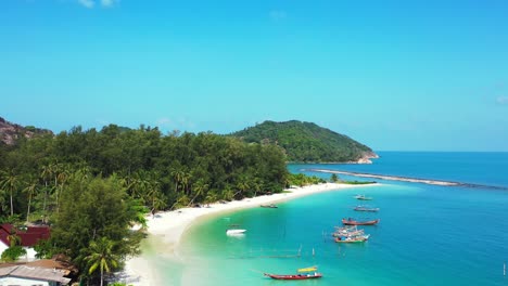 Calm-bay-of-tropical-island-with-white-sandy-beach-under-palm-trees,-washed-by-turquoise-lagoon-full-of-anchored-boats-in-Thailand