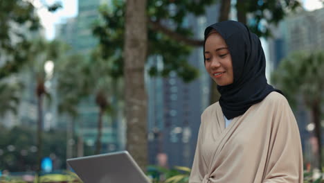 young muslim woman working on laptop in urban park