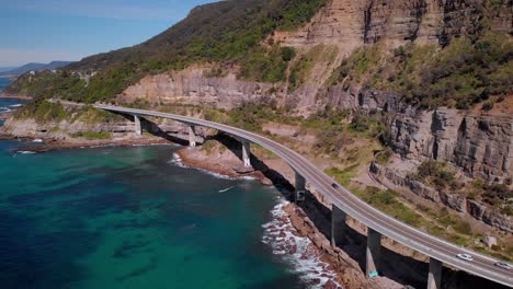 aerial view of sea cliff bridge, sunny day, grand pacific drive, new south wales, australia - backward drone shot reveal