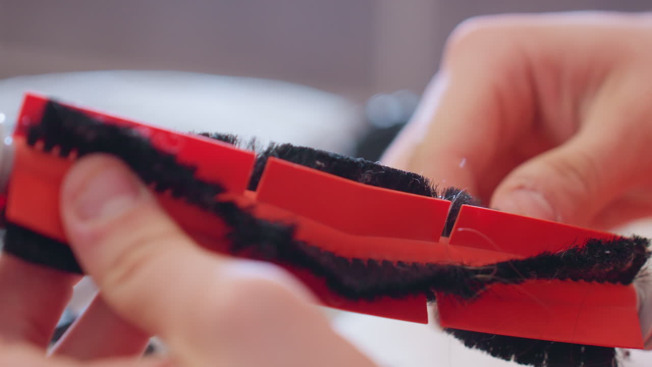 Close up of hands removing tangled hair from vacuum cleaner rotating brush during repair process to maintain efficiency, improve cleaning performance