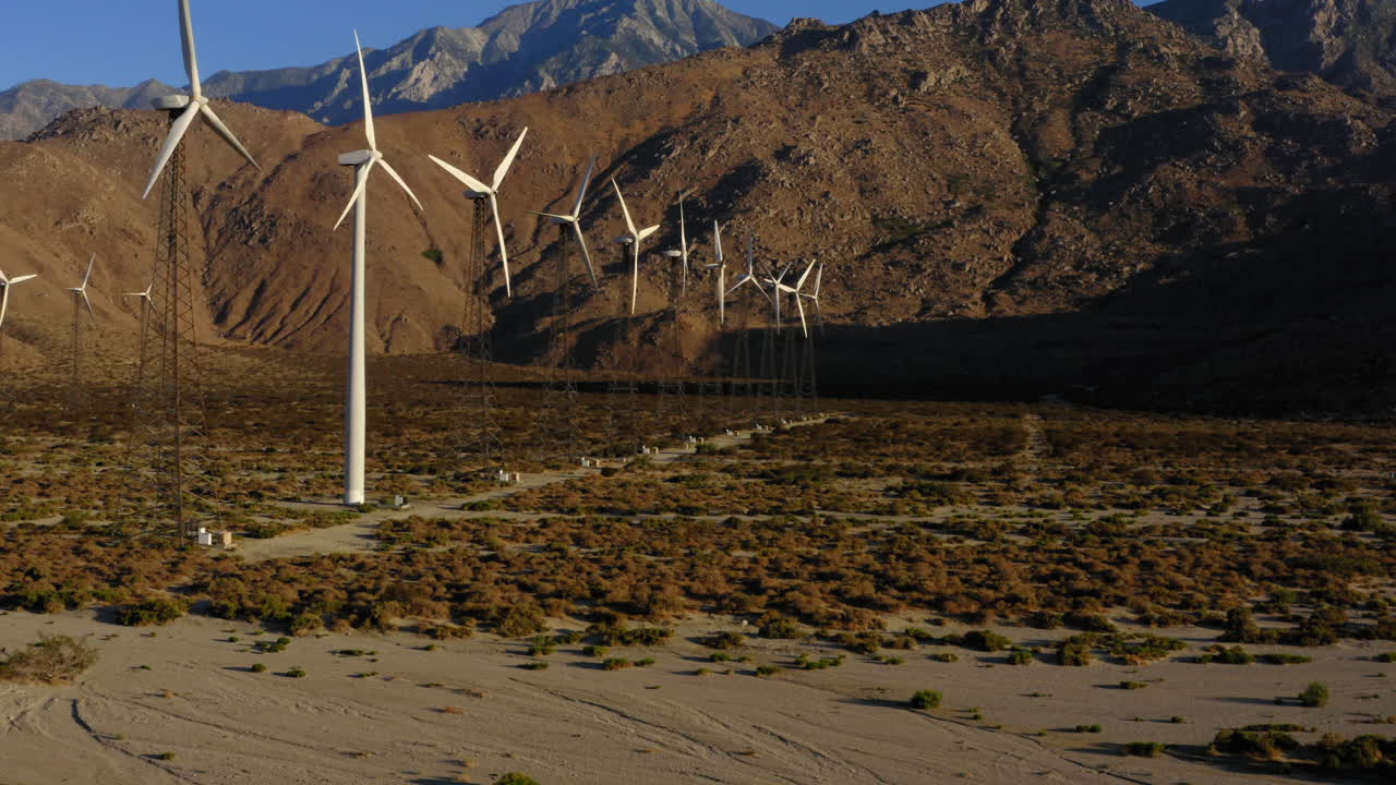 vista aérea panorámica de izquierda a derecha con vistas a las turbinas eólicas alineadas, el desierto y las enormes montañas cerca de palm springs en el desierto de mojave, california, ee.uu.