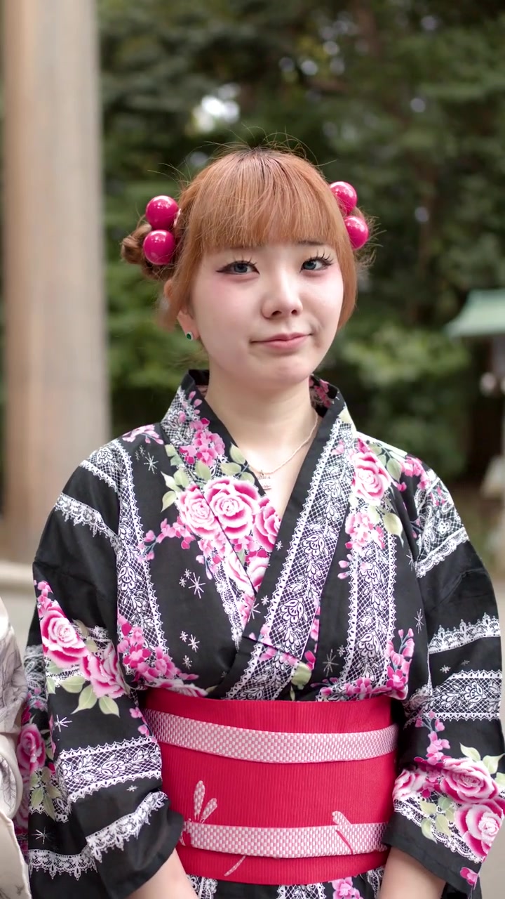 東京の神社の外に立つ、花柄の浴衣を着た若い日本人女性