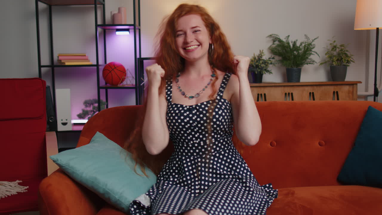 mujer pelirroja celebrando el éxito, ganar, logro de la meta, buenas noticias, suerte de la lotería en la habitación de casa