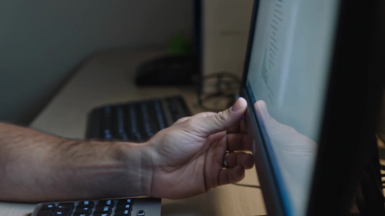 Sykepleier i blå uniform sjekker skjerm, rekker frem og trykker på knapp ved klinikkens skranke for bedre oversikt.