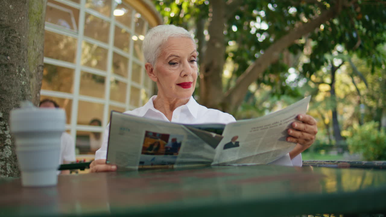 Mature lady looking magazine enjoying summer morning in open air cafe closeup.