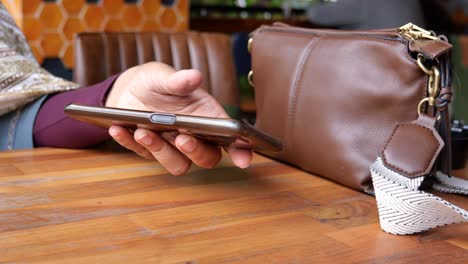 woman using phone at a cafe with her bag