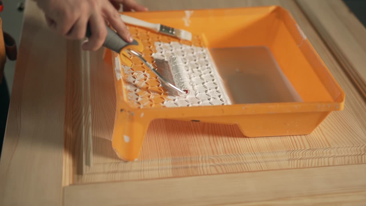 primer plano de manos masculinas con rodillo de pintura y bandeja