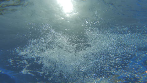 underwater view at a person jumping into a blue pool on a sunny day with bubles