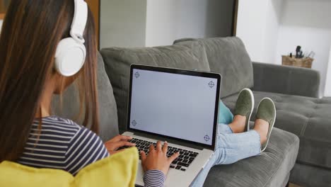 A-biracial-teenager-girl-with-headphones-using-laptop-with-copy-space-at-home,-slow-motion