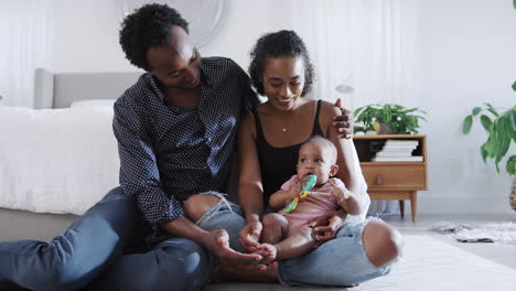 Loving-Parents-Playing-With-Baby-Daughter-Sitting-On-Floor-In-Bedroom