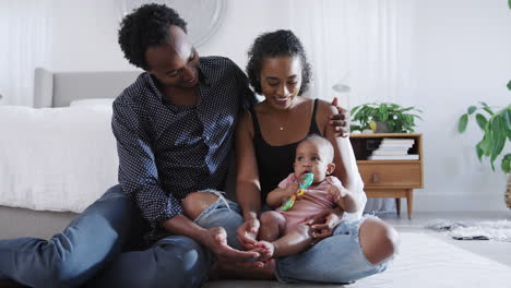 loving parents playing with baby daughter sitting on floor in bedroom