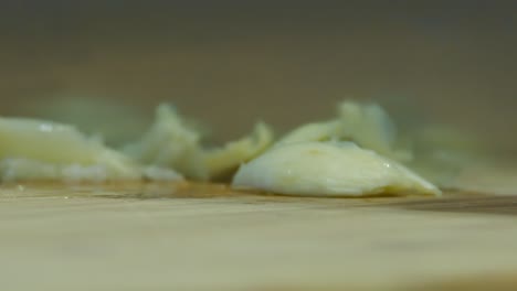 Extreme-closeup:-Knife-chops-cloves-of-garlic-on-wooden-cutting-board