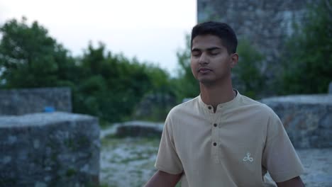 push-in shot of indian man in deep meditation at dawn while sitting amongst castle ruins on top of the hill