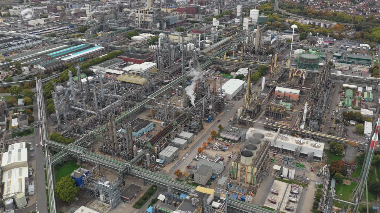 Imagens aéreas expansivas exibindo um vasto complexo industrial com tubulações intrincadas, torres e tanques de armazenamento para refino químico e de petróleo.