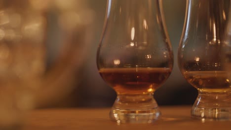Two whiskey glasses with amber liquid sit on a wooden surface, illuminated by soft, warm candlelight. Slow horizontal camera pan creates a cozy, intimate mood