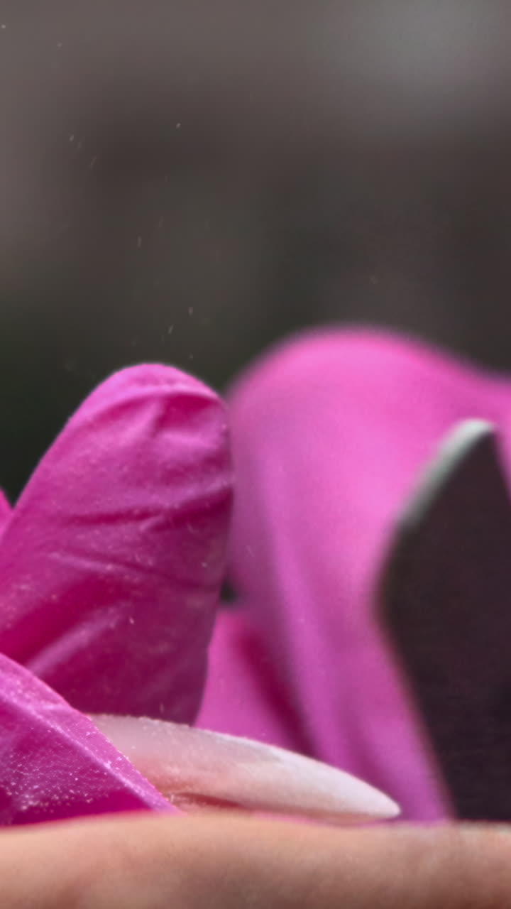 Primo piano di una mano con guanto rosa che lima un'unghia
