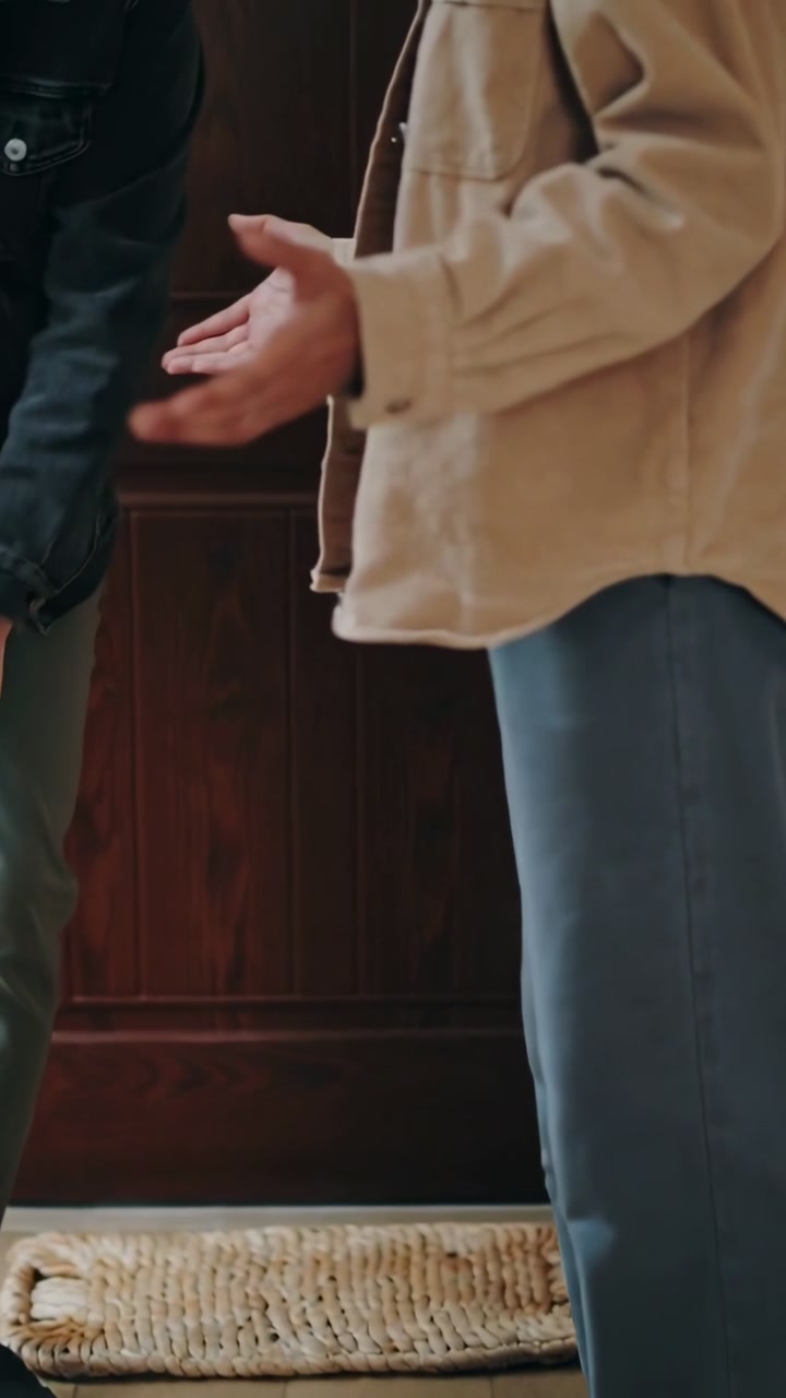 Vertical video: Arriving man shifting near front door, woman in corduroy gesturing explaining plans
