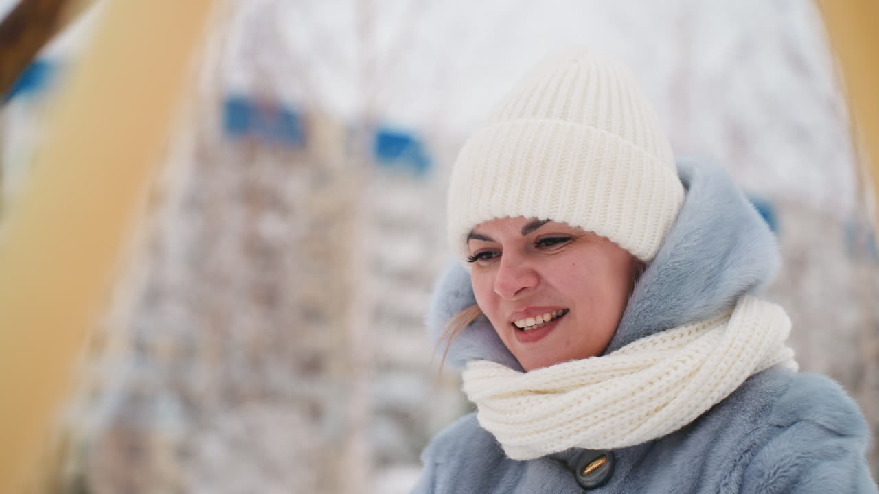 Caucasian woman on playground swing smiling, knit beanie and chunky scarf against snowy park and apartment skyline, bright candid laughter, rosy cheeks and cozy coat, joyful winter mood, casual