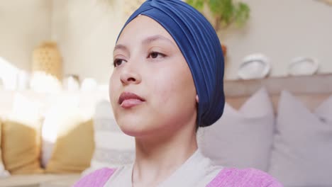 video of tranquil biracial woman in hijab doing yoga meditation, closing eyes and deep breathing