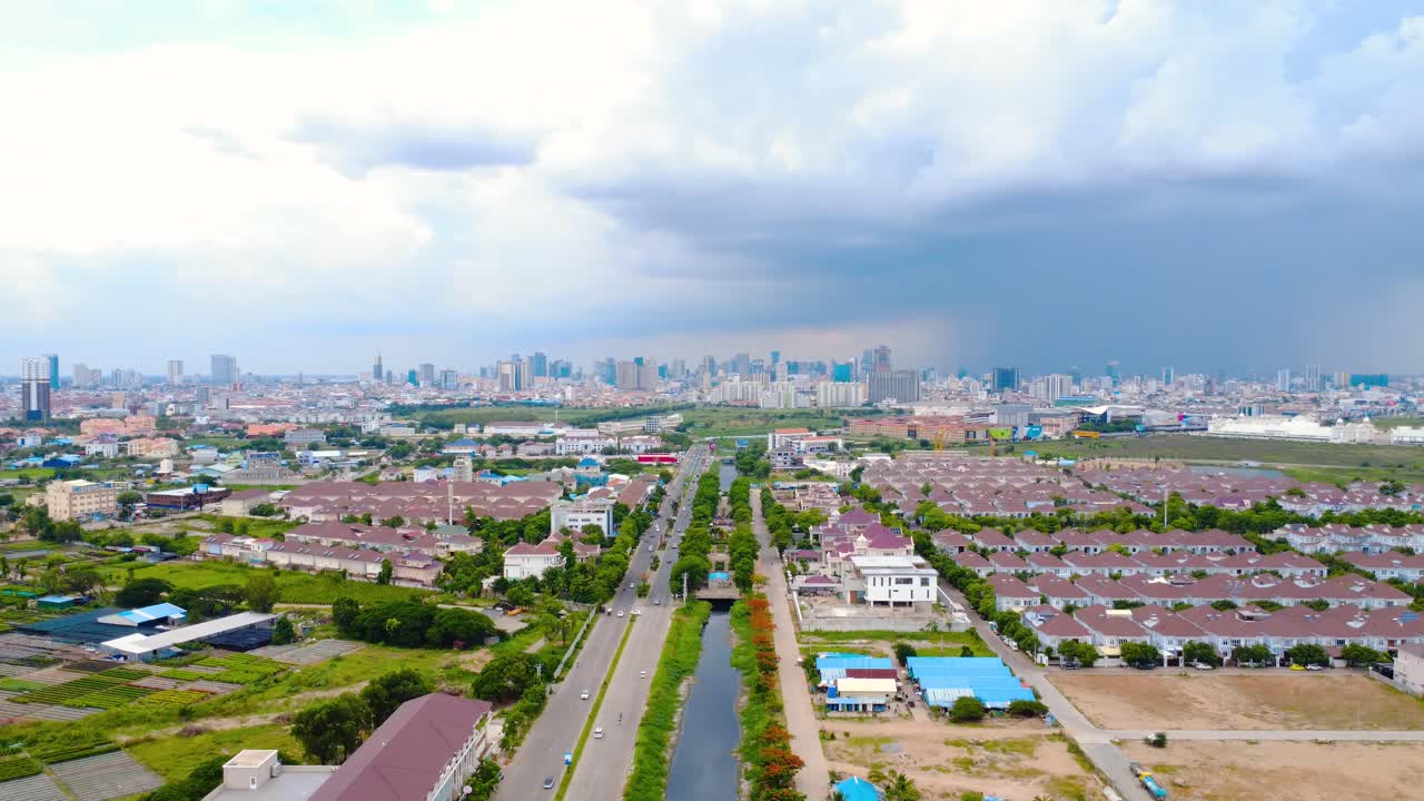 Aerial footage of Phnom Penh's sprawling cityscape under dramatic cloud cover. Captivating bird's eye view, vibrant greens and urban layout under moody skies.