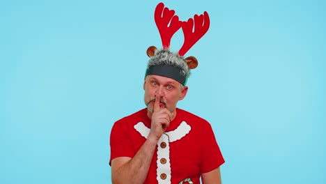 hombre usa camiseta roja de navidad presiona el dedo índice a los labios hace silencio gesto signo, secreto