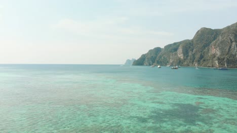 Shallow-warm-Emerald-green-sea-covering-the-vastness-of-Ko-Phi-Phi-Don-Island-Coast-in-Thailand---Aerial-Backwards-Fly-over-shot