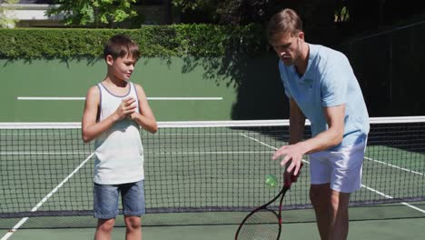 caucasian father teaching his son to play tennis at tennis court on a bright sunny day