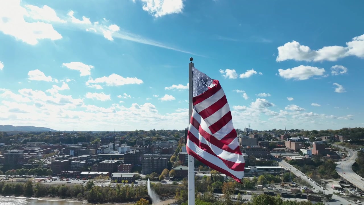 Bandiera americana patriottica su pennone che sventola sulla città. Giornata di sole in una città americana in autunno. Orbita aerea ravvicinata. Centro città con edifici per uffici sullo sfondo. Paesaggio colorato del Connecticut.