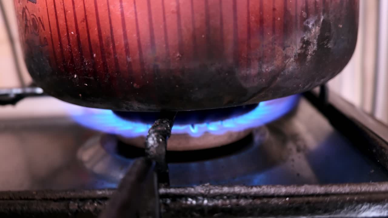 Primer plano detallado de una olla de metal calentándose sobre la llama azul de una estufa de gas en una cocina interior, destacando el calor de cocción, los utensilios de cocina domésticos, el detalle del quemador y el uso de electrodomésticos