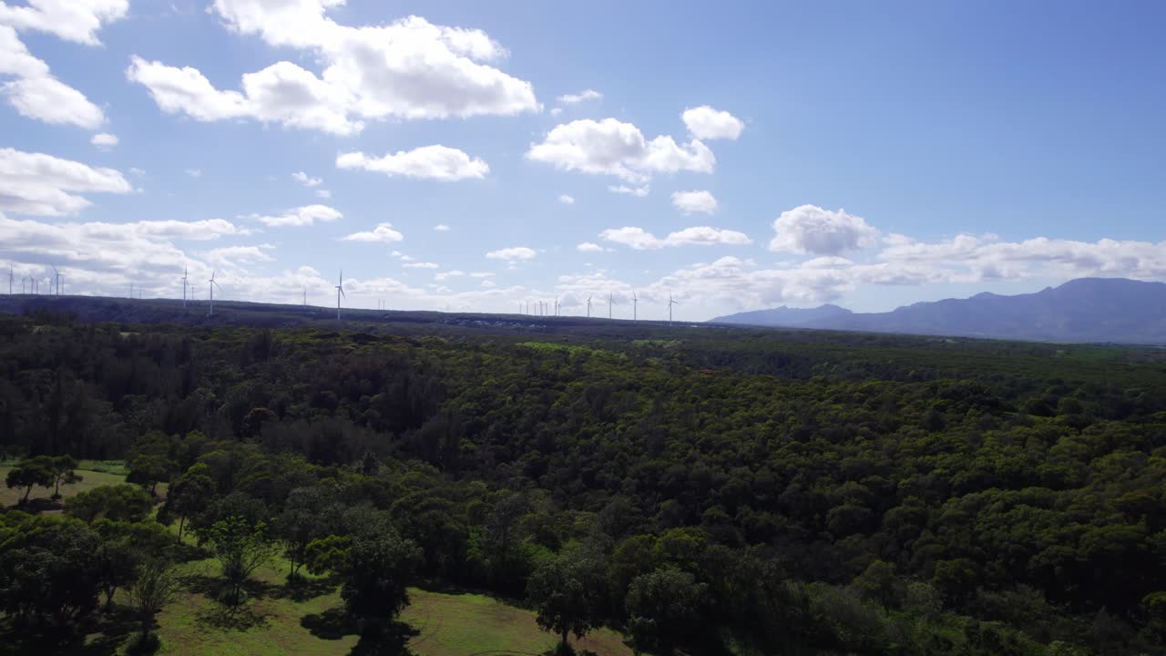 Riprese con drone vicino alla costa nord di Oahu, Hawaii, con lussureggianti montagne verdi e mulini a vento per energia verde che punteggiano l'orizzonte.