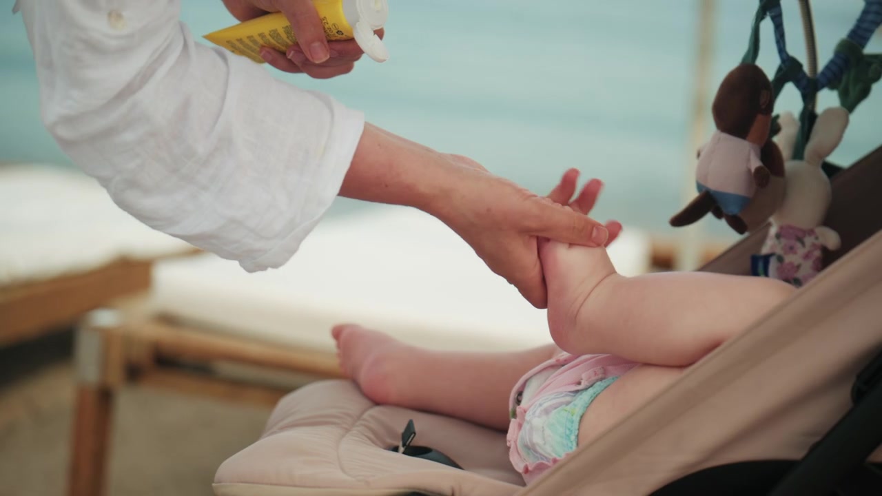 Close up of a mother applying sunscreen lotion on baby skin at beach during sunny day