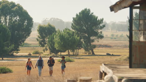 Grupo-De-Amigos-Con-Mochilas-Caminando-Juntos-En-El-Campo