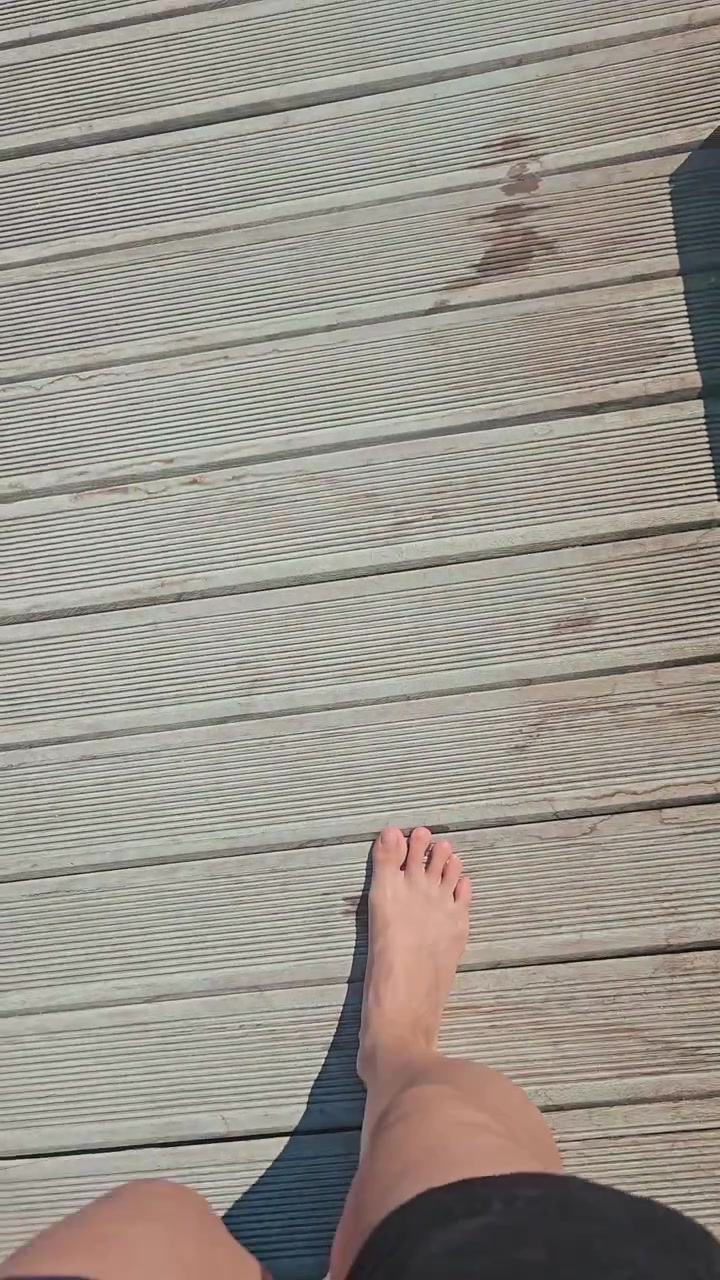POV di una donna che cammina su un ponte di legno o una passerella in un hotel, resort sulla spiaggia o sul ponte bagnato di una barca, durante una vacanza estiva all'aperto. Si gode la vacanza al mare o all'oceano. Ripreso con la fotocamera del telefono in stile reel UGC.