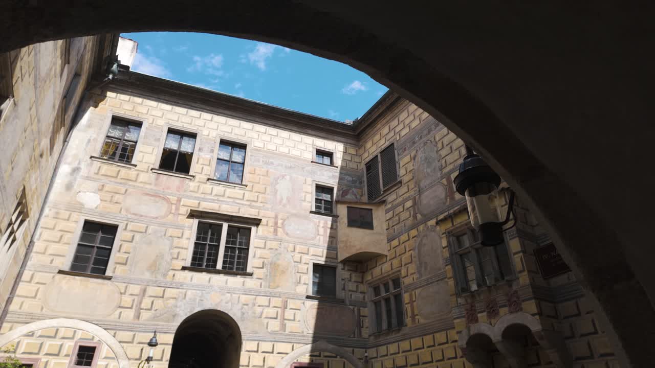 Courtyard of the historic Český Krumlov Castle under a blue sky viewed through an archway