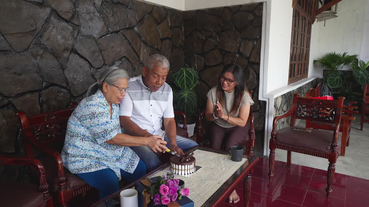 Hombre asiático mayor feliz cortando pastel y celebrando cumpleaños con su familia en casa
