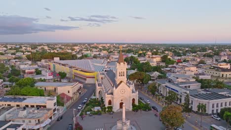 tomada aérea de la catedral de san pedro apóstol durante la hora dorada en san pedro de macoris, república dominicana - la gente en la plaza con el monumento