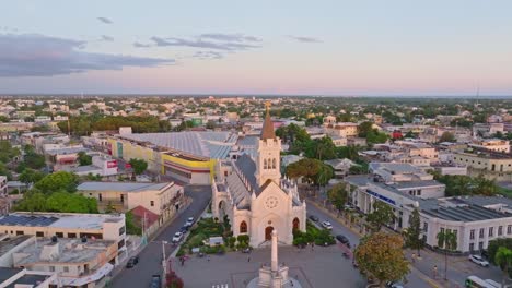 aerial orbit shot of cathedral san pedro apostol during golden hour in san pedro de macoris, dominican republic - people on square with monument