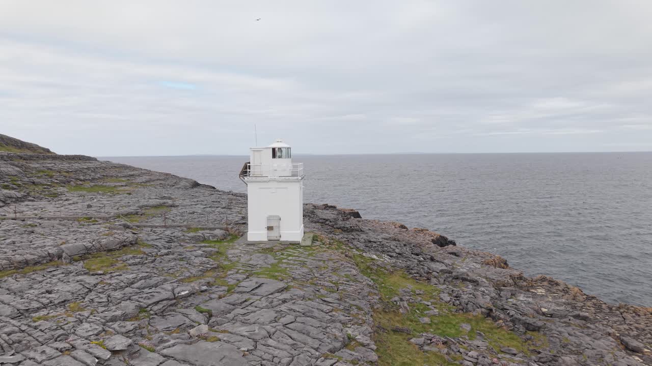Black Head Lighthouse In County Clare, Ireland - White Lighthouse On Rugged Coastline Overlooking Seascape On Cloudy Day. approaching drone shot