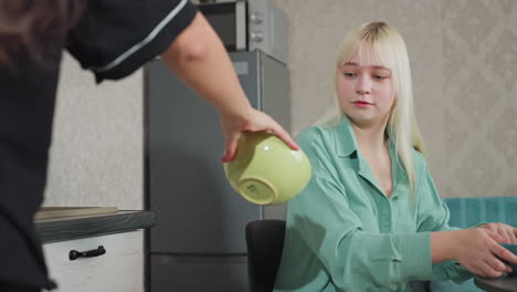 close up of lady handing ceramic bowl to sister in kitchen with fridge and microwave behind, casual home interaction between friends, bright atmosphere, modern kitchen setting, happy moment