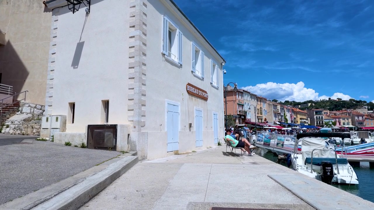 Persone che camminano e si rilassano in un soleggiato porto mediterraneo.