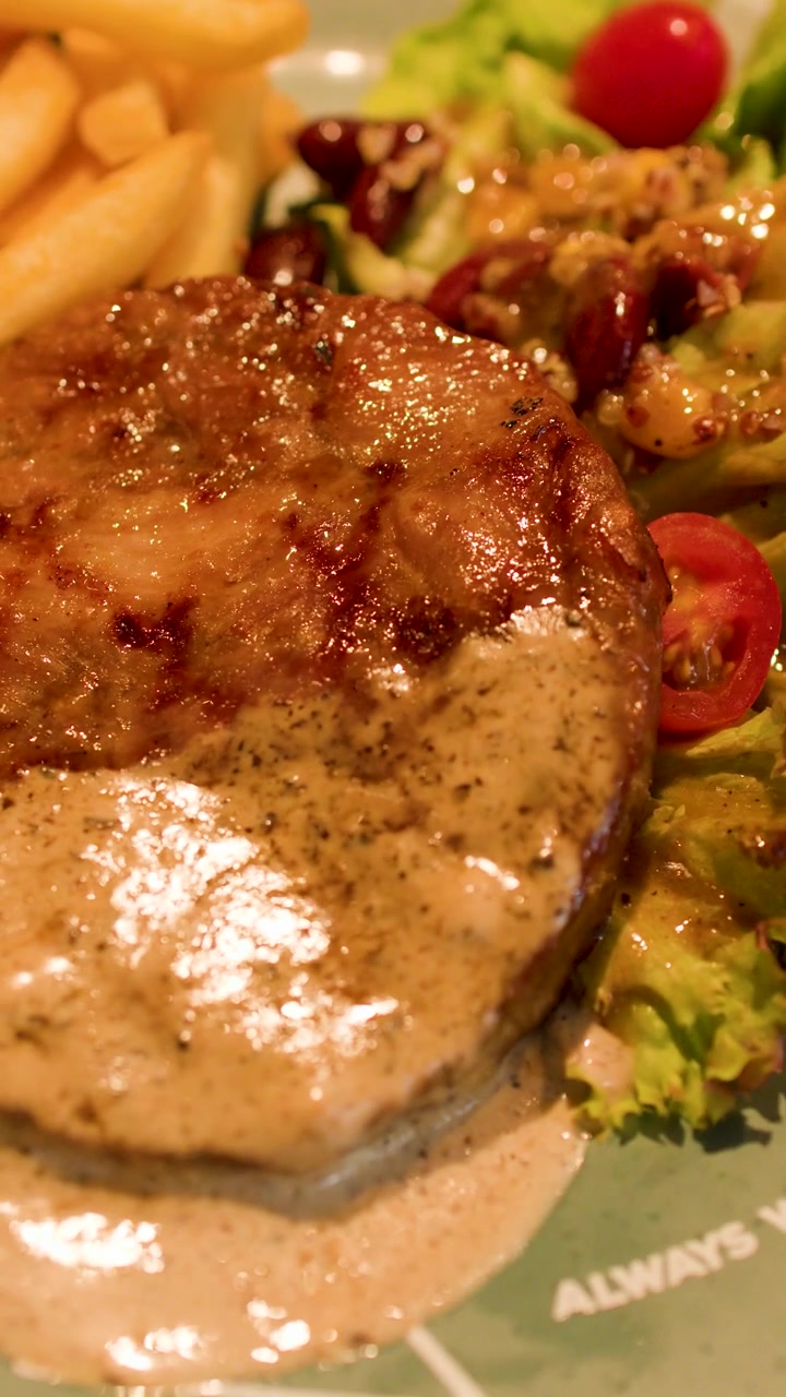 Primo piano: la telecamera scorre su una bistecca alla griglia impiattata, guarnita con salsa cremosa ai funghi e contorni.