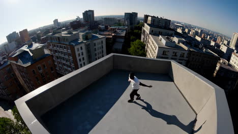 a man dancing dynamically on a concrete rooftop with a cityscape view under a clear blue sky